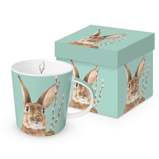 Eine Porzellantasse mit Hasenmotiv und passender Geschenkdose auf hellblauem Hintergrund.
