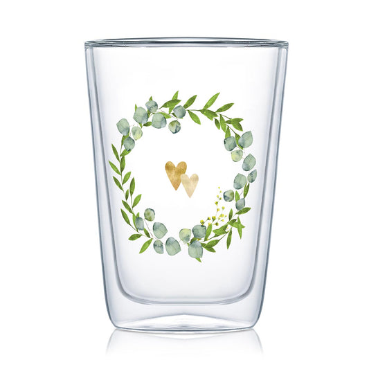 Ein doppelwandiges Glas aus Borosilikatglas mit einem Kranz aus Blättern und zwei goldenen Herzen.